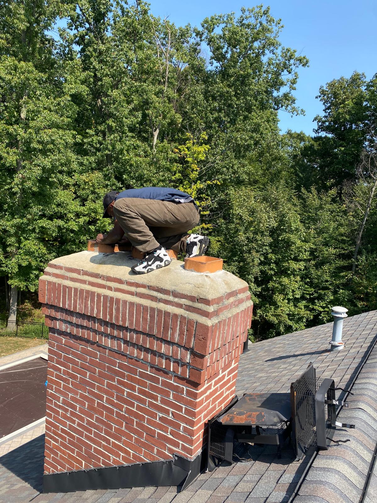 A technician leaning over the flue openings on a brick chimney