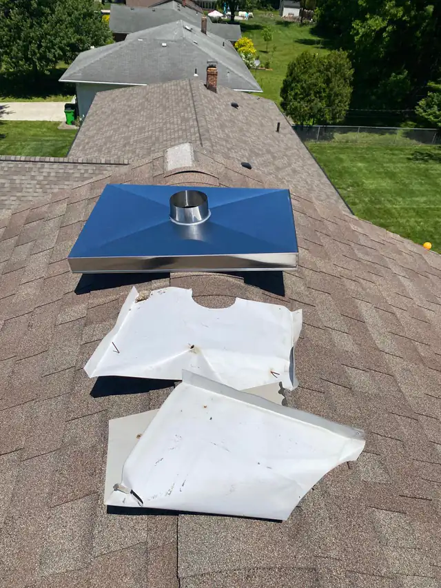 A metal replacement chase cover with a round collar resting on roof shingles beside two cut-up sections of the removed cover