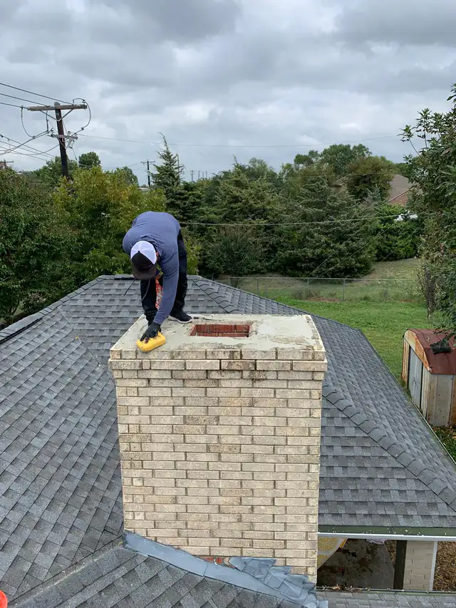 A technician finishing a freshly placed chimney crown with a sponge, the open flue visible in the new crown