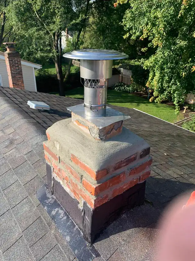 A new stainless steel chimney liner emerging through a freshly parged crown, finished with a stainless rain cap
