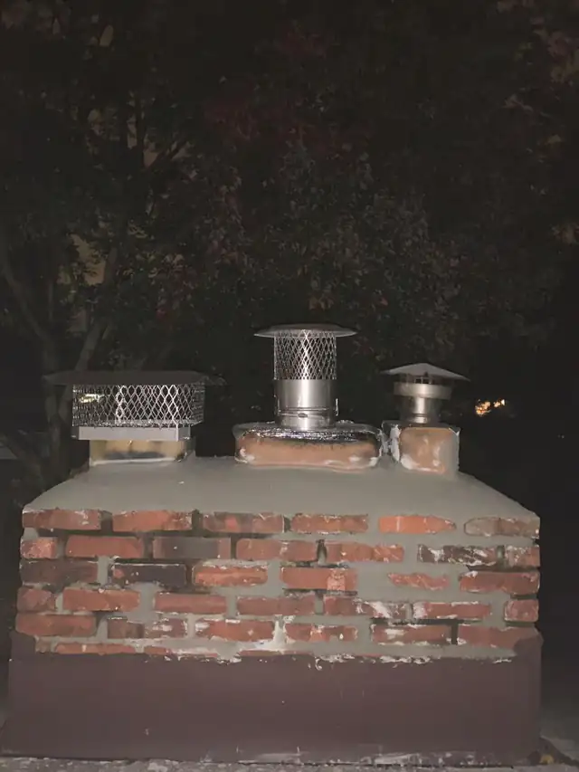 A multi-flue brick chimney with three separate stainless caps set into a newly finished crown