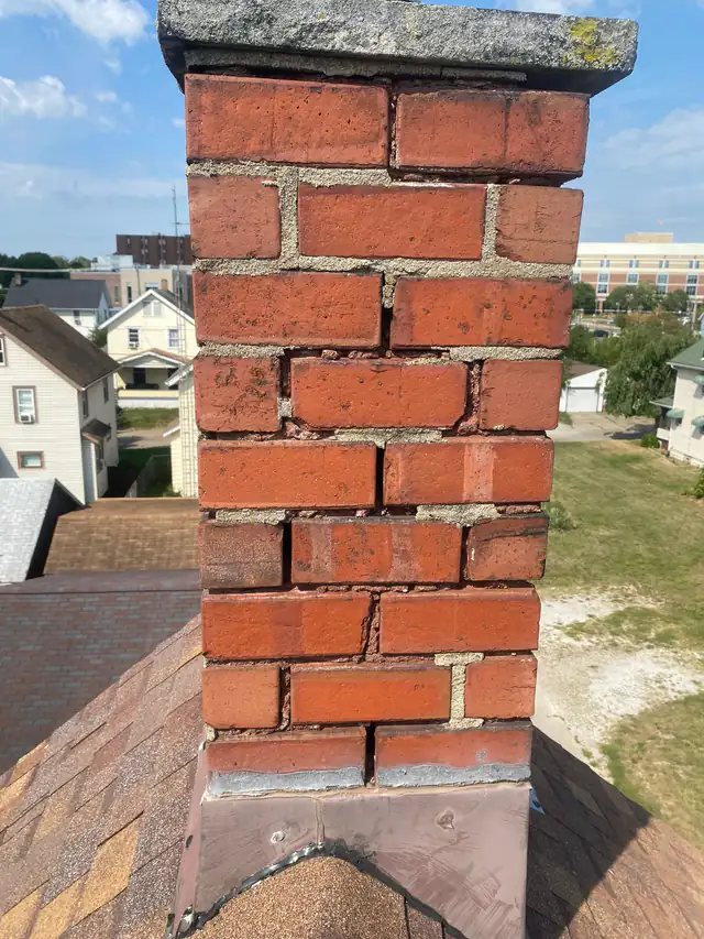 A brick chimney stack with badly eroded mortar joints — deep gaps, missing mortar and open head joints between the bricks