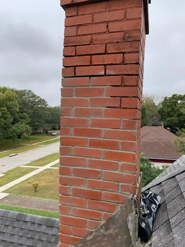 A brick chimney stack mid-repointing, with freshly packed mortar joints on the lower courses and eroded joints still open above
